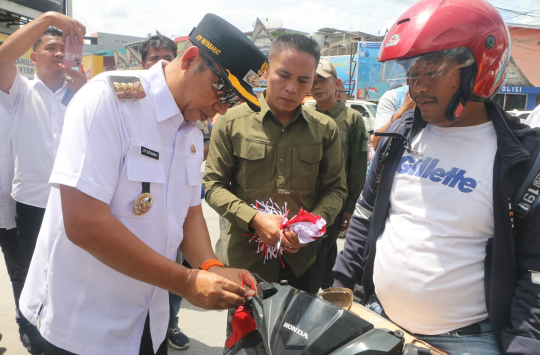 Bupati Tapanuli Utara Dr. Jonius Taripar P. Hutabarat saat menyerahkan bendera merah putih kepada masyarakat di Simpang Empat Menara Lonceng, sebagai bagian dari Gerakan Pembagian Bendera Merah Putih menyambut HUT RI ke-80. (Foto:Loksa Situmeang/Kabarnas)